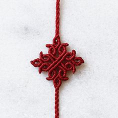 a red piece of string with an intricate design on it, sitting on a white surface