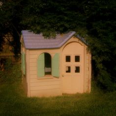 a small wooden shed sitting in the middle of a yard with green grass and trees