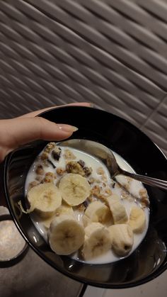 a bowl of cereal with bananas and yogurt in it is being held by a woman's hand