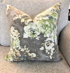 a floral pillow is sitting on a gray couch with white and green flowers in the center