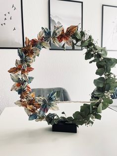 a wreath made out of leaves on top of a white table next to framed pictures