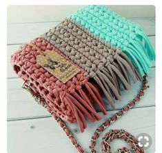 a multicolored knitted purse sitting on top of a white wooden floor next to a chain