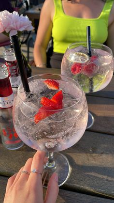 a person holding up a wine glass filled with ice and strawberries on the table