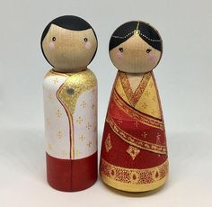 two wooden dolls sitting next to each other on a white surface with gold and red accents