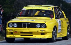 a yellow race car driving down a road with people watching from the sidelines behind it