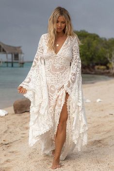 a woman is walking on the beach in a white dress