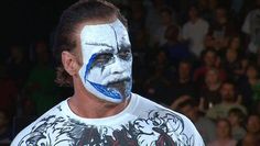 a man with his face painted white and blue is standing in front of an audience