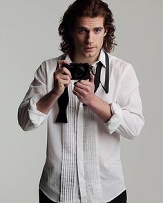 a man with long hair is holding a camera and wearing a white button up shirt