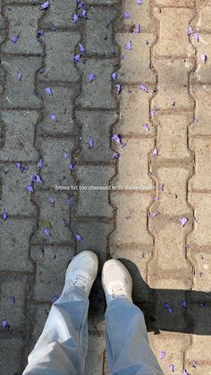 a person standing on a sidewalk with their feet up and purple flowers scattered all over the ground