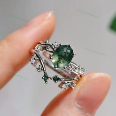 a person is holding a ring with green stones and leaves on it's side