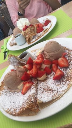 two white plates topped with pancakes covered in powdered sugar and strawberries