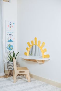 a yellow sun shaped mirror sitting on top of a wall next to a wooden stool