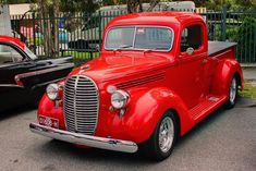 an old red truck parked next to a black car in front of a gated area