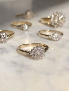 five different types of diamond rings on a marble counter top, with one being surrounded by smaller diamonds