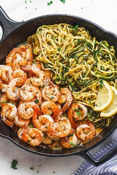 shrimp and pasta in a skillet with lemon wedges