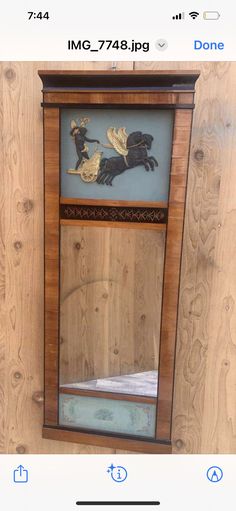 an old wooden mirror with a black dog on it's face and gold trim