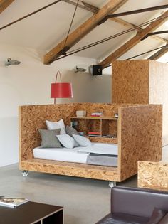 a bed made out of plywood in a room with leather chairs and a red lamp