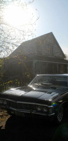 an old black car parked in front of a house with the sun shining on it