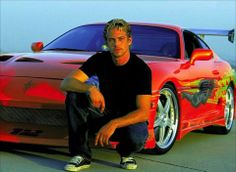 a man sitting on the ground next to a red sports car with flames painted on it