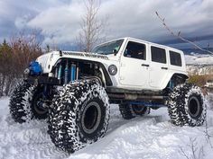 a white four - door jeep driving through the snow with monster wheels on it's tires