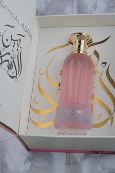 an open box with a pink bottle in it on a marble table top next to a gold and white design