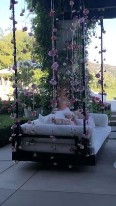 a white couch sitting on top of a patio next to a lush green hillside covered in pink flowers