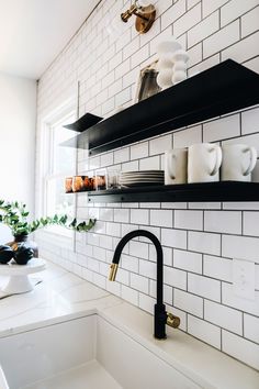 a kitchen with white tile and black shelving above the sink, along with shelves on the wall