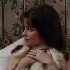 the woman is wearing a fur coat and holding her hands on her chest while sitting in bed