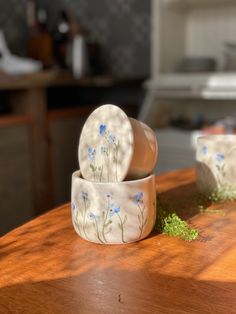 two bowls sitting on top of a wooden table covered in grass and blue daisies