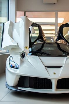 a white sports car is parked in a building with its doors open and it's hood up