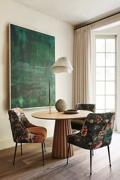 a dining room table with chairs and a large painting on the wall behind it in front of two windows