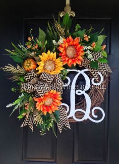 a monogrammed wreath on the front door with flowers and leaves hanging from it