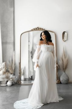 a pregnant woman standing in front of a mirror wearing a white dress with long sleeves