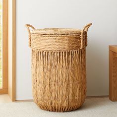 a large woven basket sitting on the floor next to a wooden table and window sill