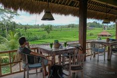 a man sitting at a table on top of a wooden floor next to a lush green field