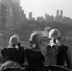 three women sitting on top of a building looking out at the city skyline in black and white