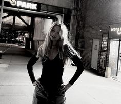 a woman standing on the sidewalk in front of a parking garage with her hands on her hips