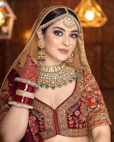 a woman in a red and gold bridal outfit with jewelry on her neck, wearing a