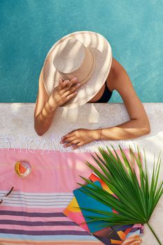 a woman laying on top of a beach towel next to a pool wearing a hat