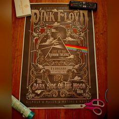 a pink floyd concert poster on a table next to some scissors and toothbrushes