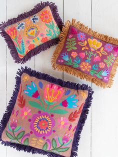 three decorative pillows with fringes on them sitting on a white wooden floor next to each other