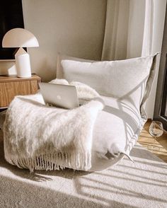 a laptop computer sitting on top of a bed next to a lamp and window sill