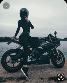 a woman sitting on top of a motorcycle next to the water and holding her helmet