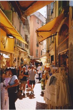 people are walking through an outdoor market with yellow umbrellas