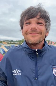 a man with grey hair and a blue jacket smiles at the camera while standing in front of tents