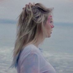 a woman with her hair blowing in the wind by the ocean on a cloudy day