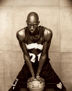 a man holding a basketball in his right hand and sitting on the floor next to a wall