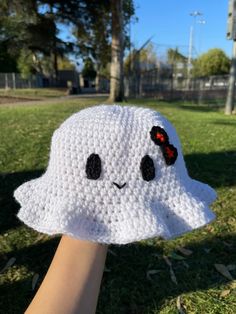 a hand holding up a white crocheted hat with black eyes and ears on it