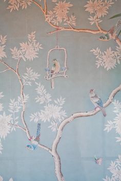 birds are sitting on the branches of a tree in front of a blue wall with white flowers