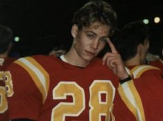 a young man in a football uniform holding his finger to his temple's ear